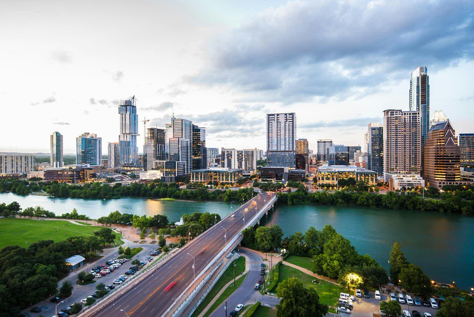 A downtown skyline behind a bridge over green water at dusk