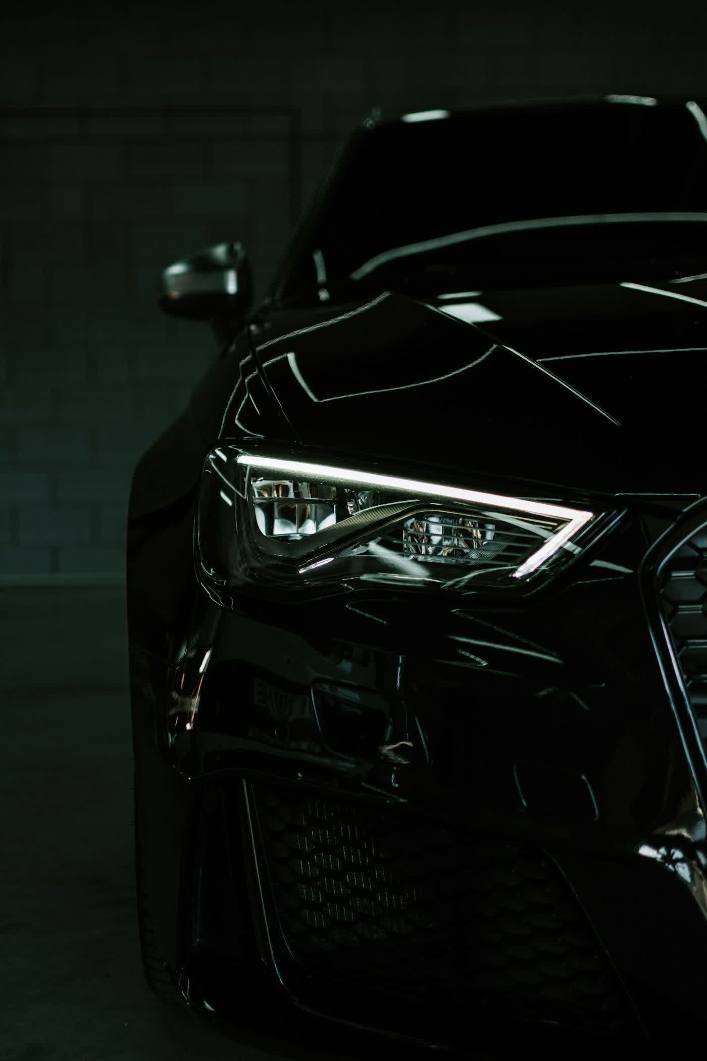 The front corner and lit headlight of a black car in the bay
