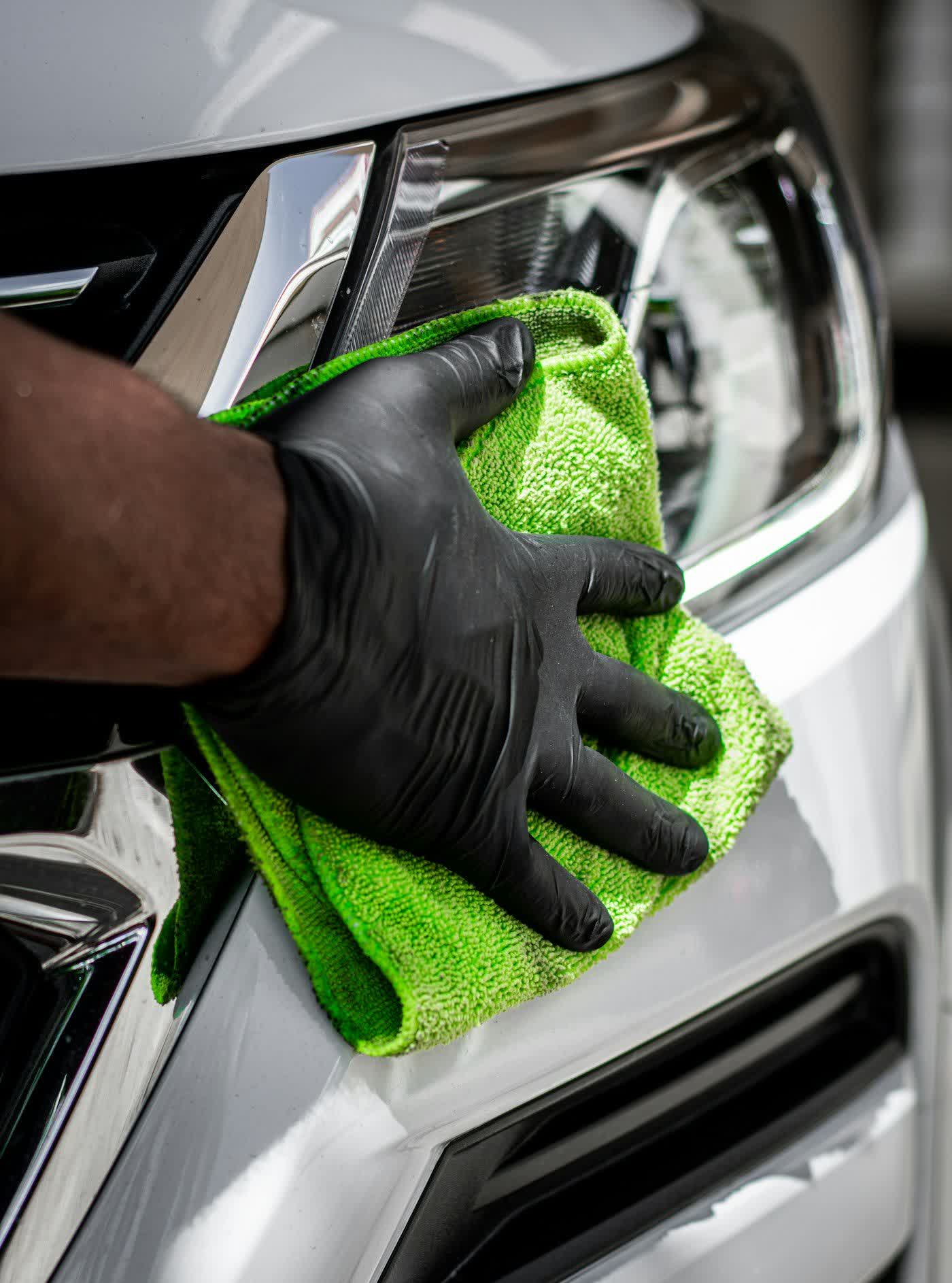 A gloved hand drying a white panel with a green microfiber towel