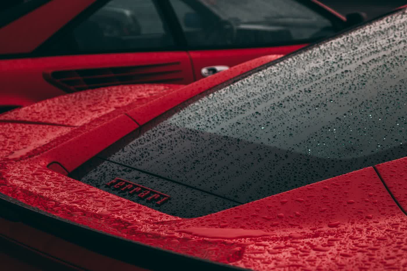 Water standing in beads across the red hood and windshield of a coated car