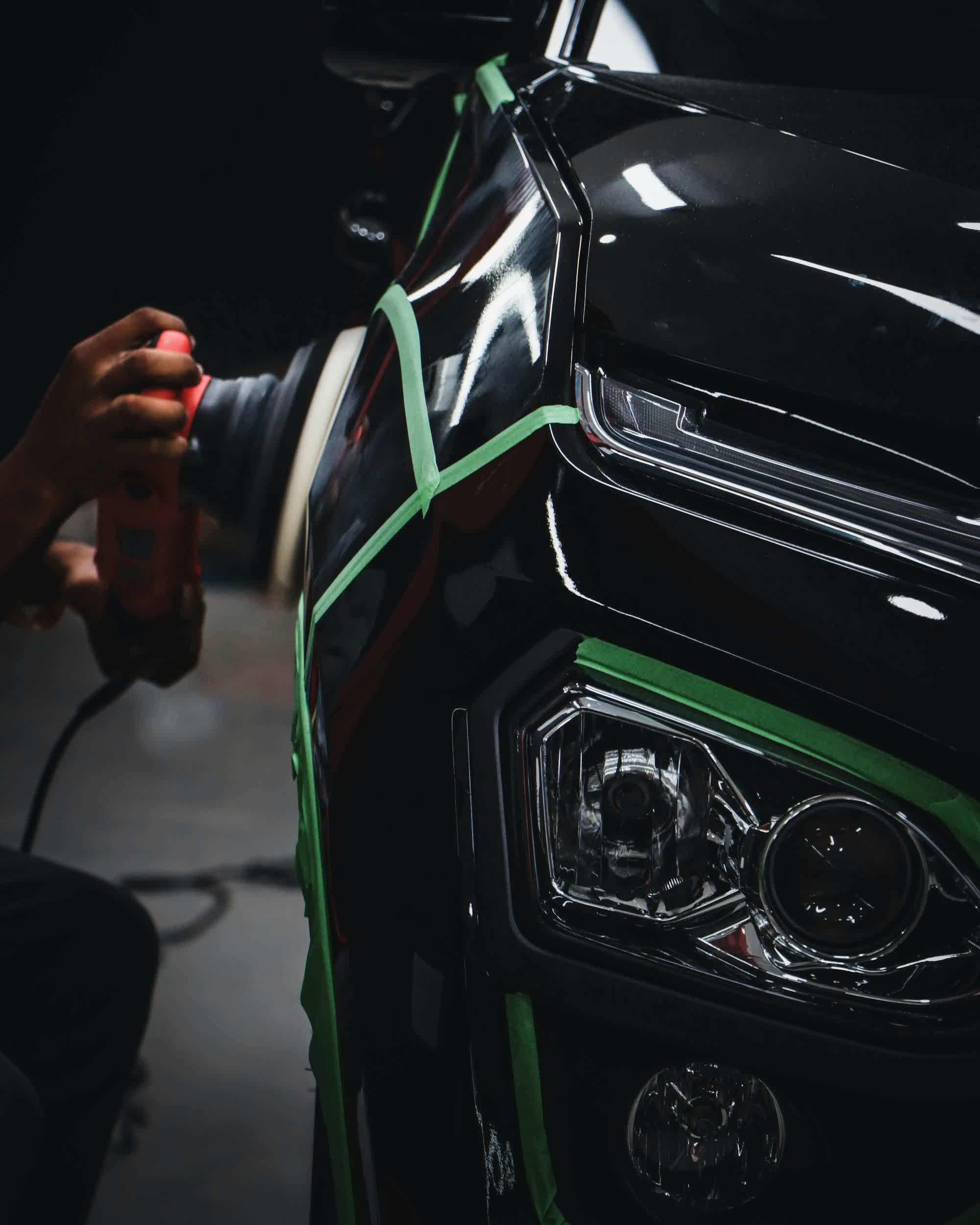 A polisher held beside the masked headlight of a black car