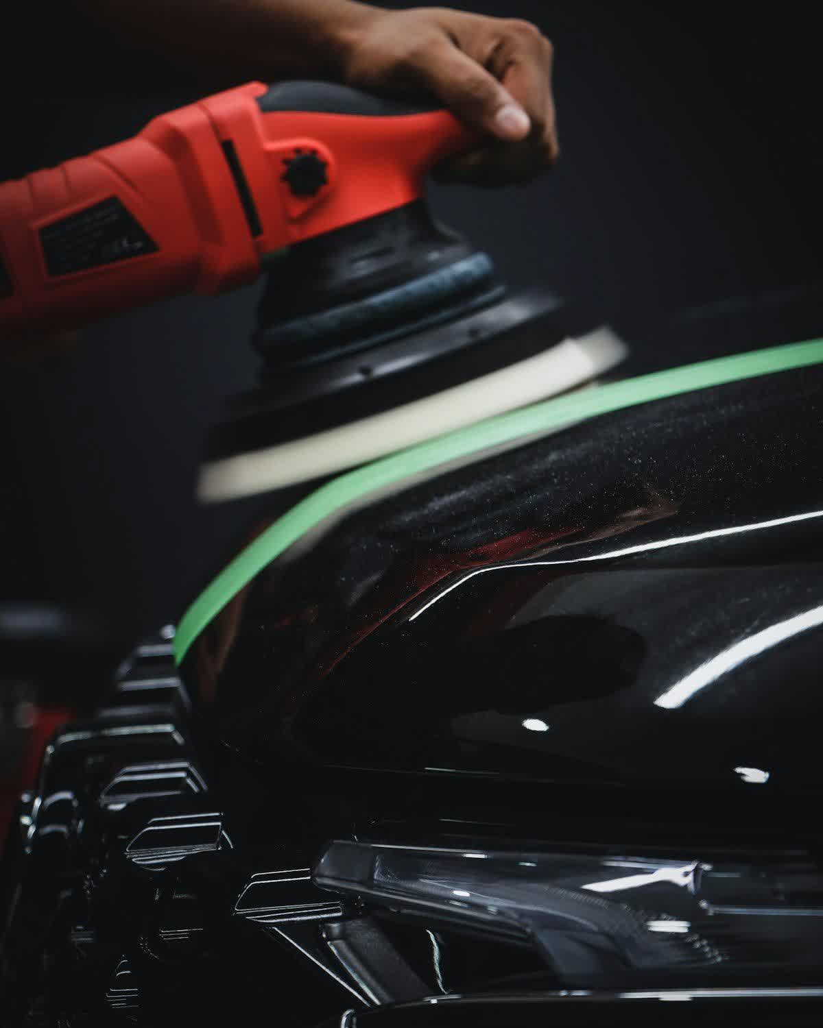 A rotary polisher held against the masked front of a black car
