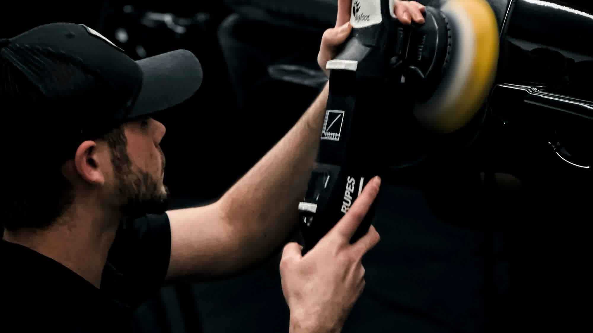 A technician holding a dual-action polisher against a dark panel
