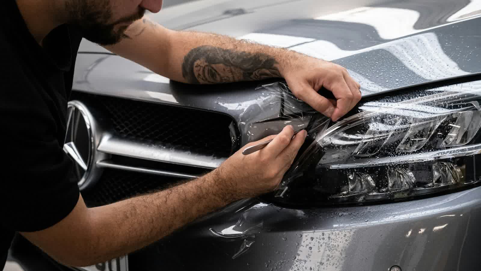 A technician pressing protection film around the headlight of a silver car