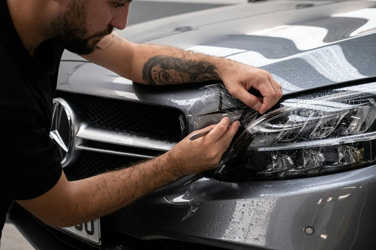 A technician pressing protection film around a headlight and grille